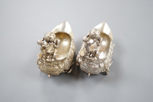 A pair of late 19th/early 20th century Hanau white metal salts, modelled as boat's with wheels and putti surmounts, maker Stork & Sinsheimer, length 81mm, 195 grams.